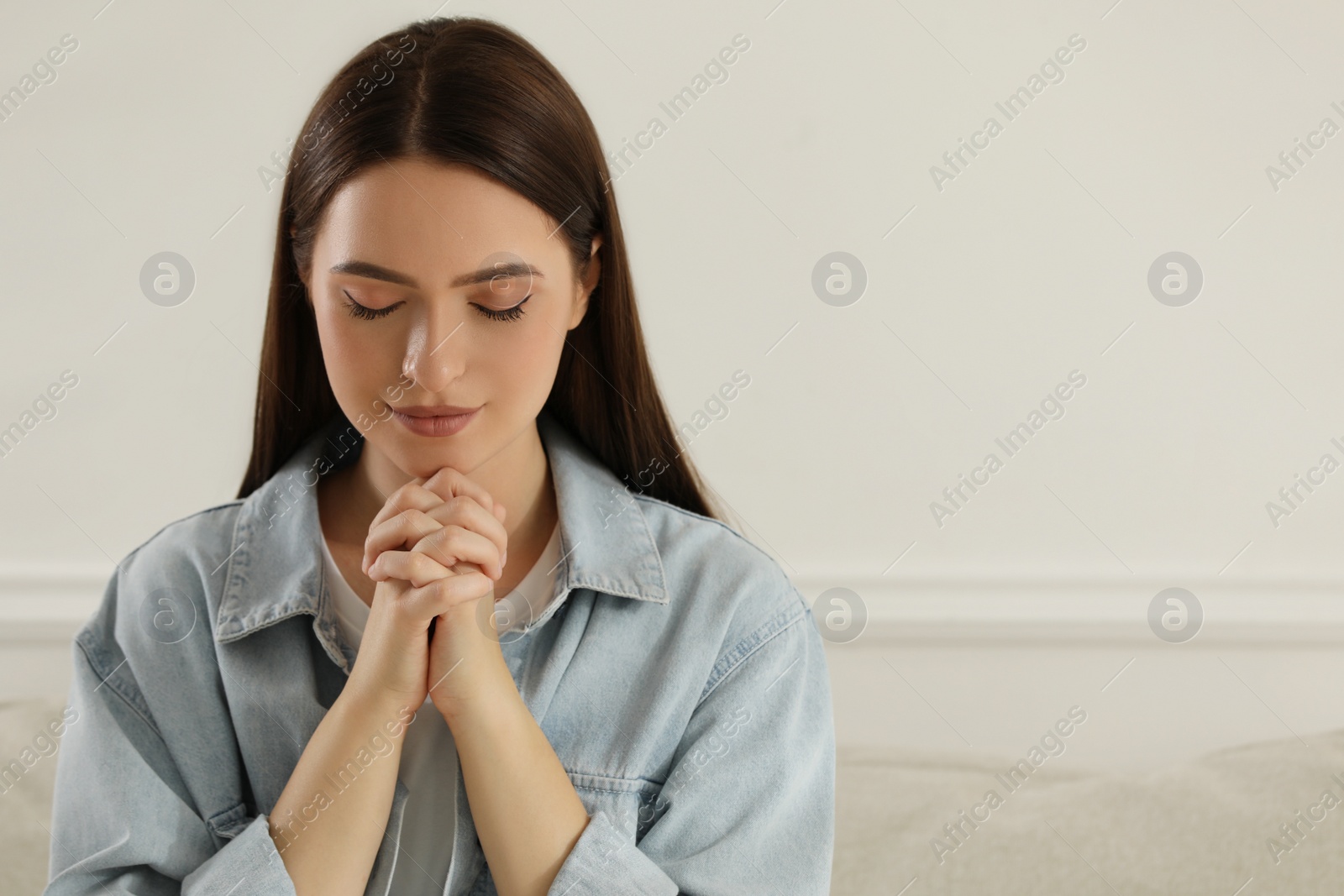 Photo of Religious young woman with clasped hands praying indoors