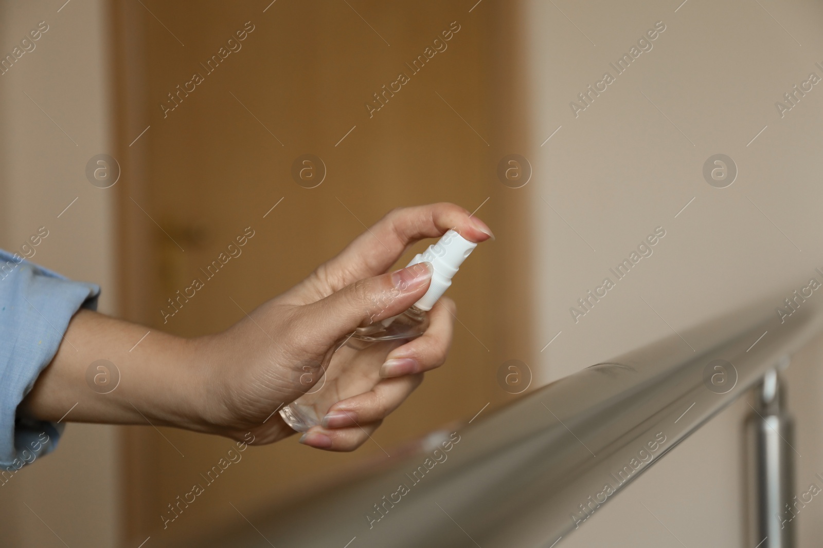 Photo of Woman spraying antiseptic onto metal railing indoors, closeup