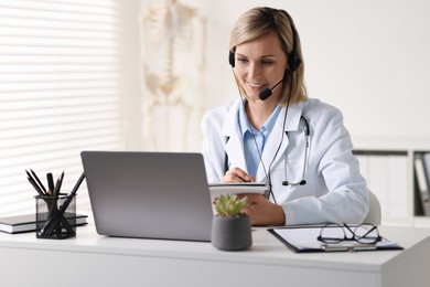 Smiling doctor with laptop having online consultation at table in office