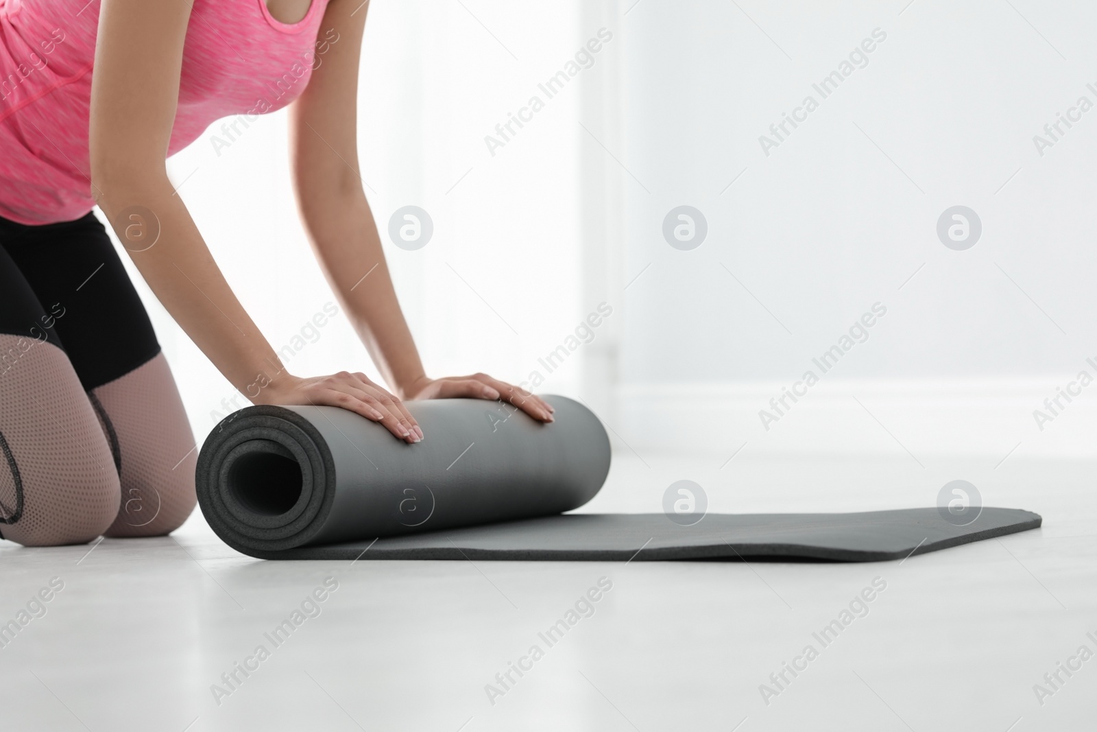 Photo of Young woman rolling yoga mat indoors, closeup. Space for text