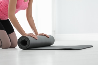 Photo of Young woman rolling yoga mat indoors, closeup. Space for text