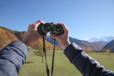 Photo of Boy holding binoculars in beautiful mountains on sunny day, closeup