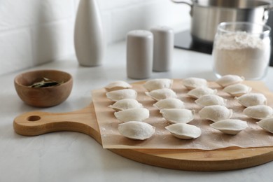 Photo of Fresh uncooked dumplings and flour on white table