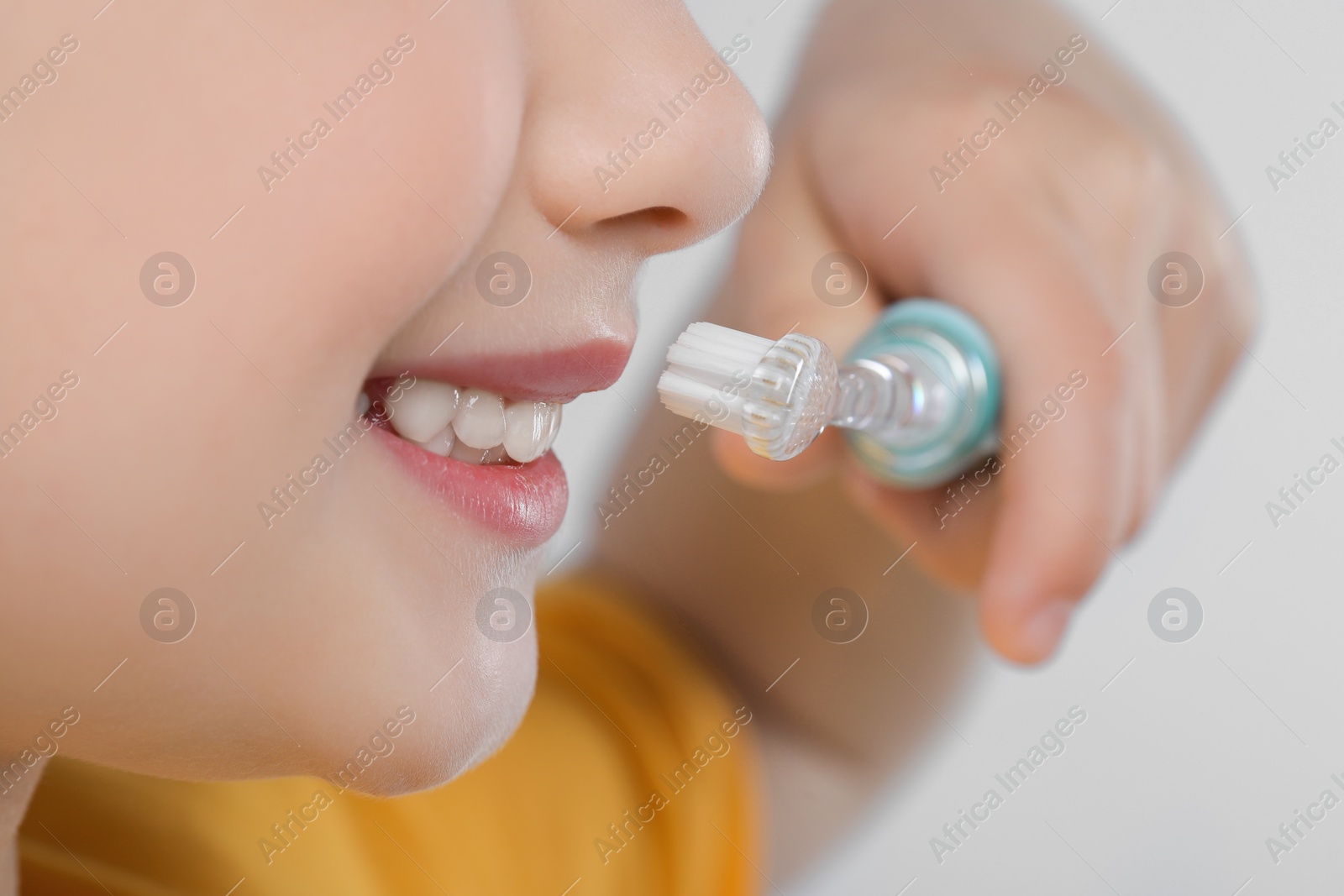 Photo of Girl brushing her teeth with electric toothbrush on light grey background, closeup