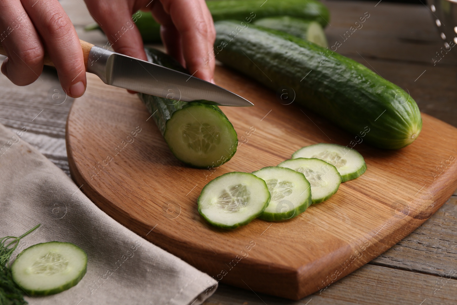 Photo of Woman cutting cucumber on wooden board at table, closeup