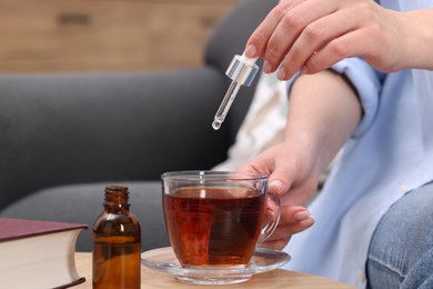 Woman dripping food supplement into cup of tea at wooden table indoors, closeup