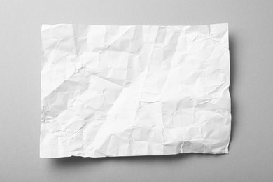 Sheet of white crumpled paper on grey background, top view