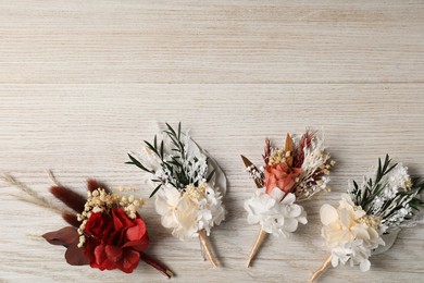 Photo of Stylish boutonnieres on white wooden table, flat lay. Space for text