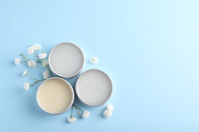 Different lip balms and gypsophila on light blue background, flat lay. Space for text