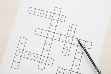 Crossword with answers and pen on white wooden table, top view