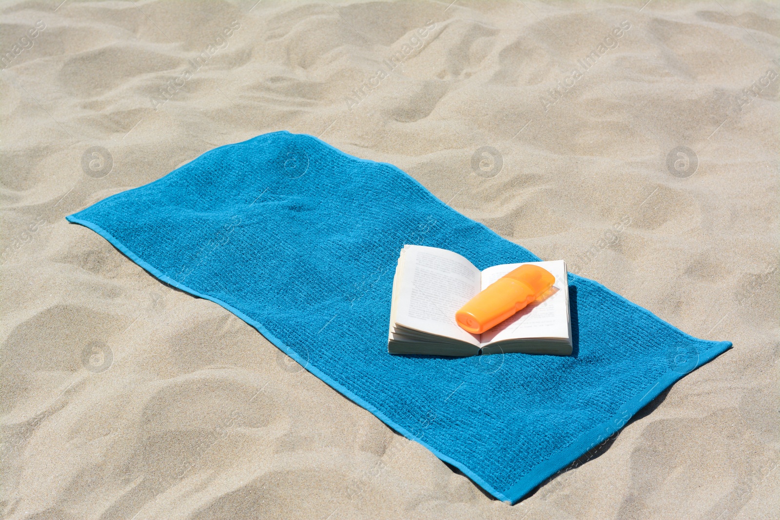 Photo of Blue towel, book and sunscreen on sandy beach