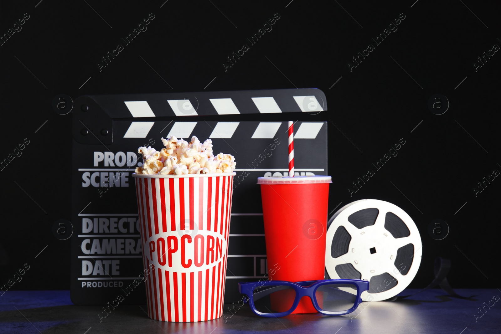 Photo of Clapperboard, reel and popcorn on table against dark background. Watching cinema