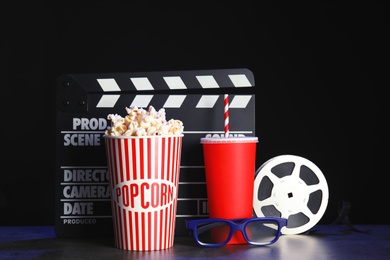 Photo of Clapperboard, reel and popcorn on table against dark background. Watching cinema