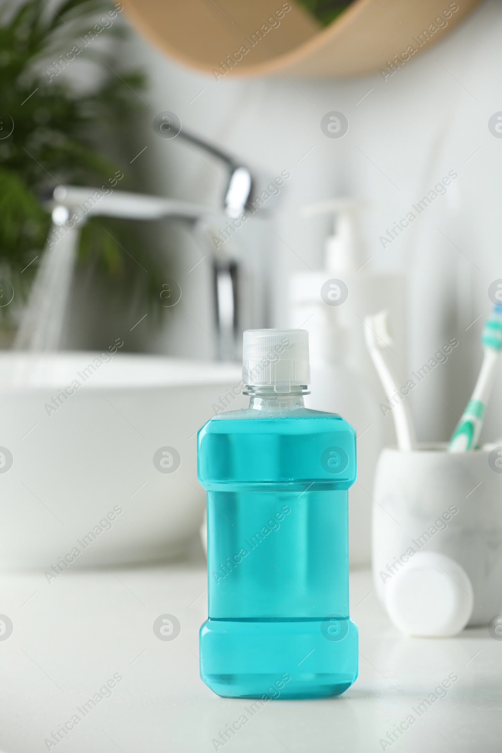 Photo of Mouthwash, toothbrushes and dental floss on white countertop in bathroom
