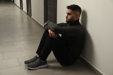 Photo of Sad man sitting on floor in hall. Space for text