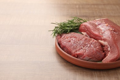 Photo of Pieces of raw beef meat with spices and rosemary on wooden table, space for text