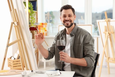Photo of Handsome man with glass of wine painting in studio. Creative hobby