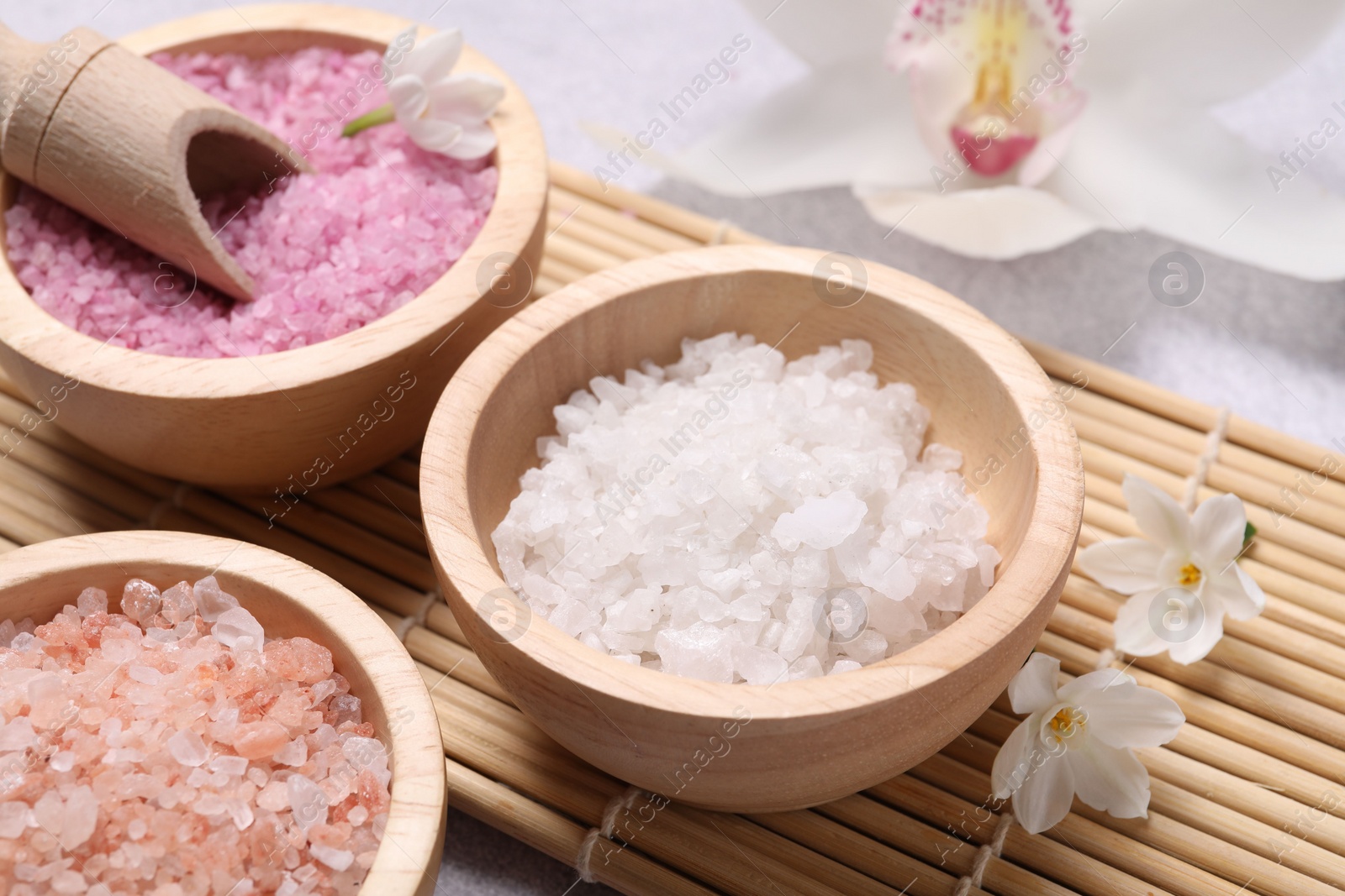 Photo of Different types of sea salt and flowers on light table, closeup. Spa products