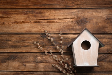 Photo of Beautiful bird house and willow branches on wooden background, flat lay. Spring composition with space for text