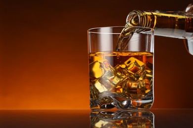 Photo of Pouring whiskey from bottle into glass at table against color background, space for text