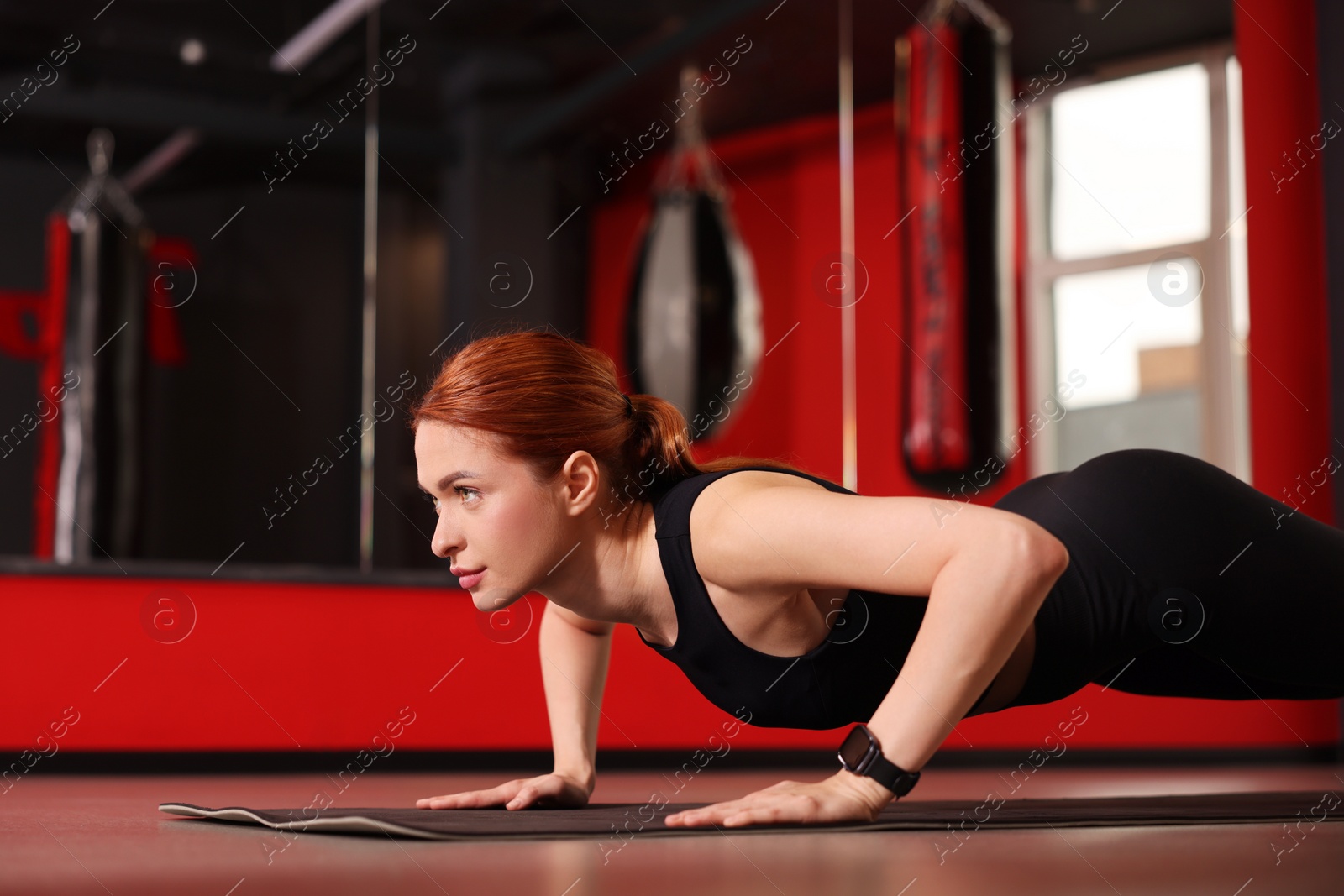 Photo of Athletic young woman doing push ups on mat in gym