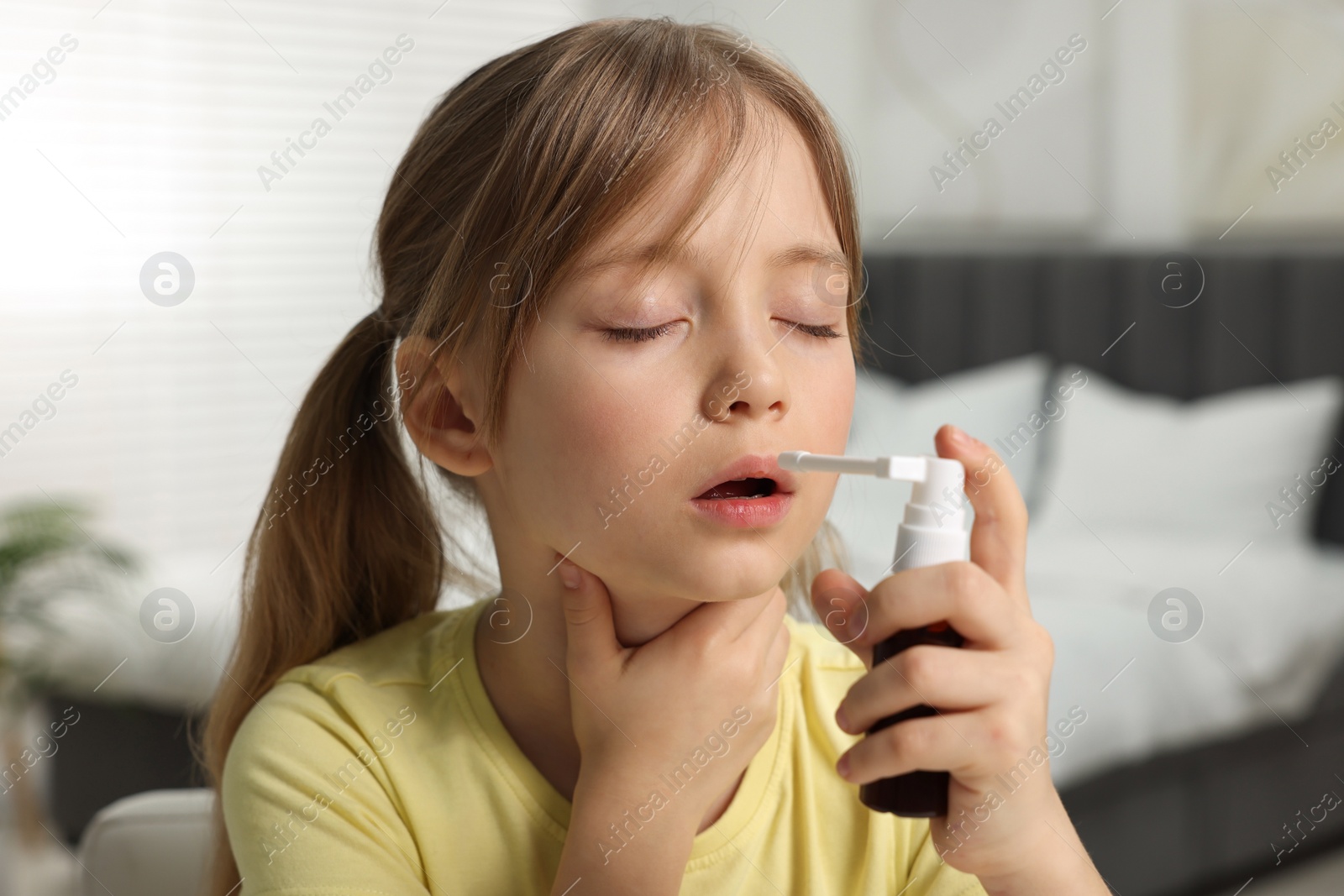 Photo of Little girl using throat spray at home