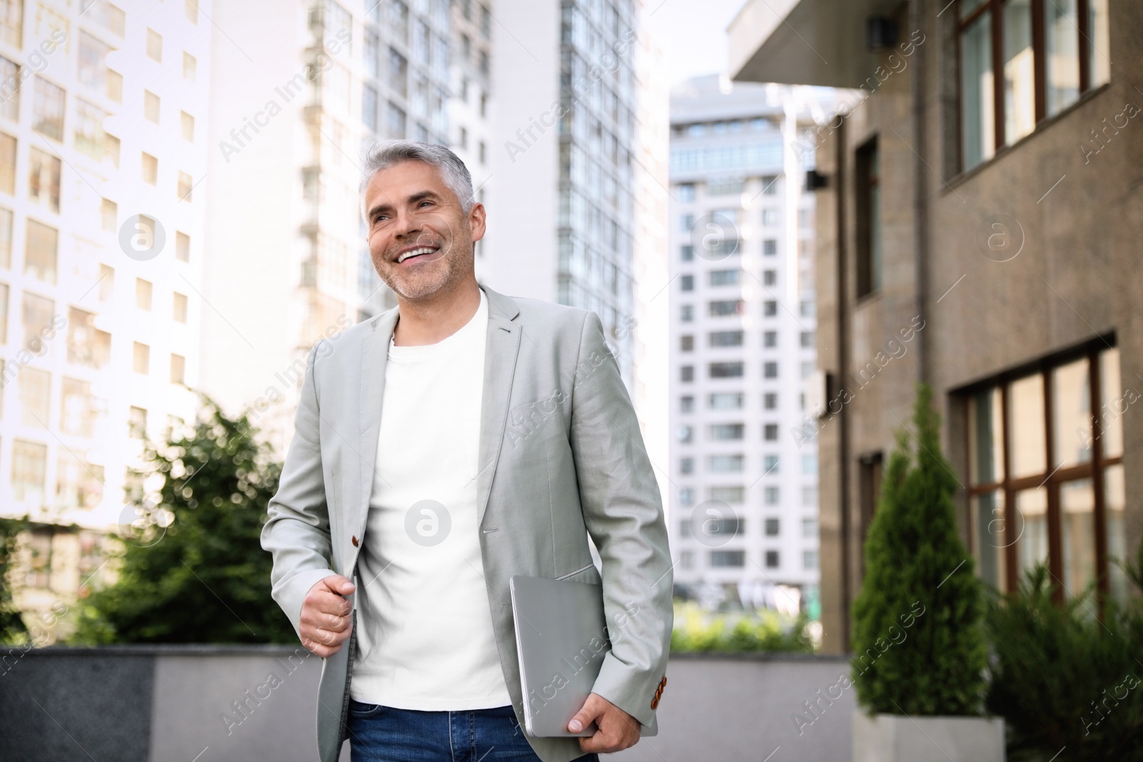 Photo of Portrait of handsome mature man with laptop in city center. Space for text