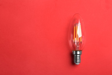 Photo of Vintage filament lamp bulb on red background, top view. Space for text