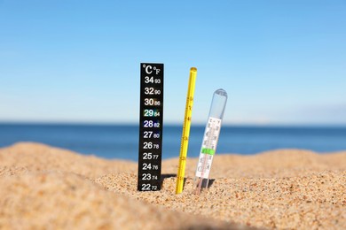 Photo of Different weather thermometers in sand near sea