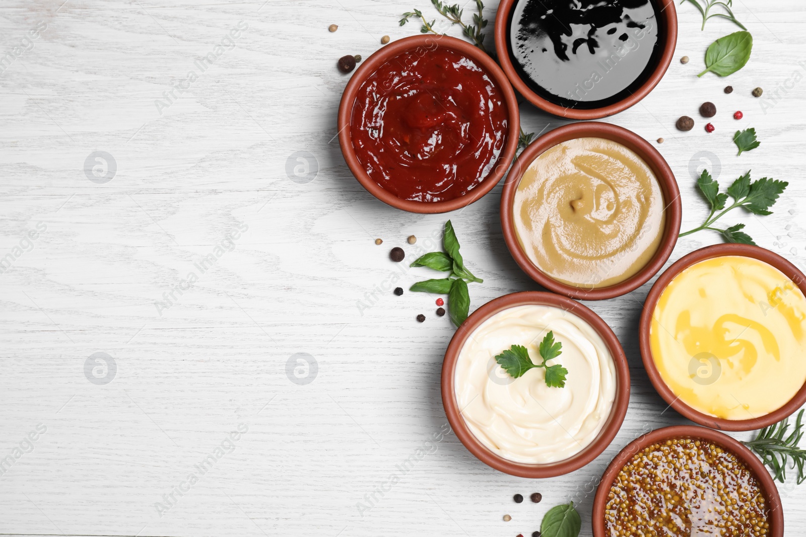 Photo of Many different sauces and herbs on white wooden table, flat lay. Space for text