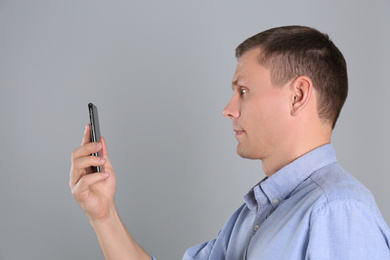 Photo of Man unlocking smartphone with facial scanner on grey background. Biometric verification