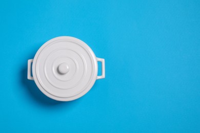 Photo of White pot with lid on light blue background, top view. Space for text