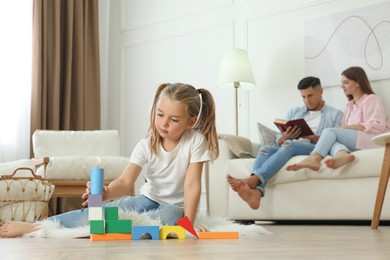 Photo of Little girl playing with colorful blocks while her parents resting on sofa at home. Floor heating concept