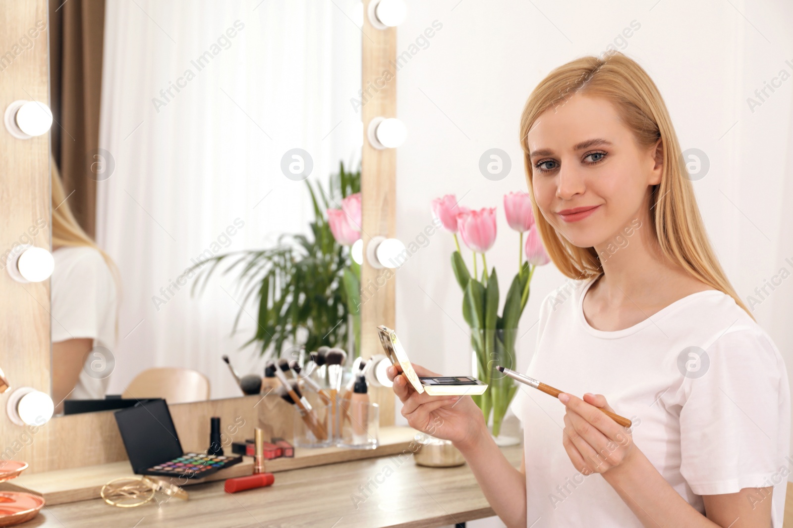 Photo of Beautiful woman applying makeup near mirror in room