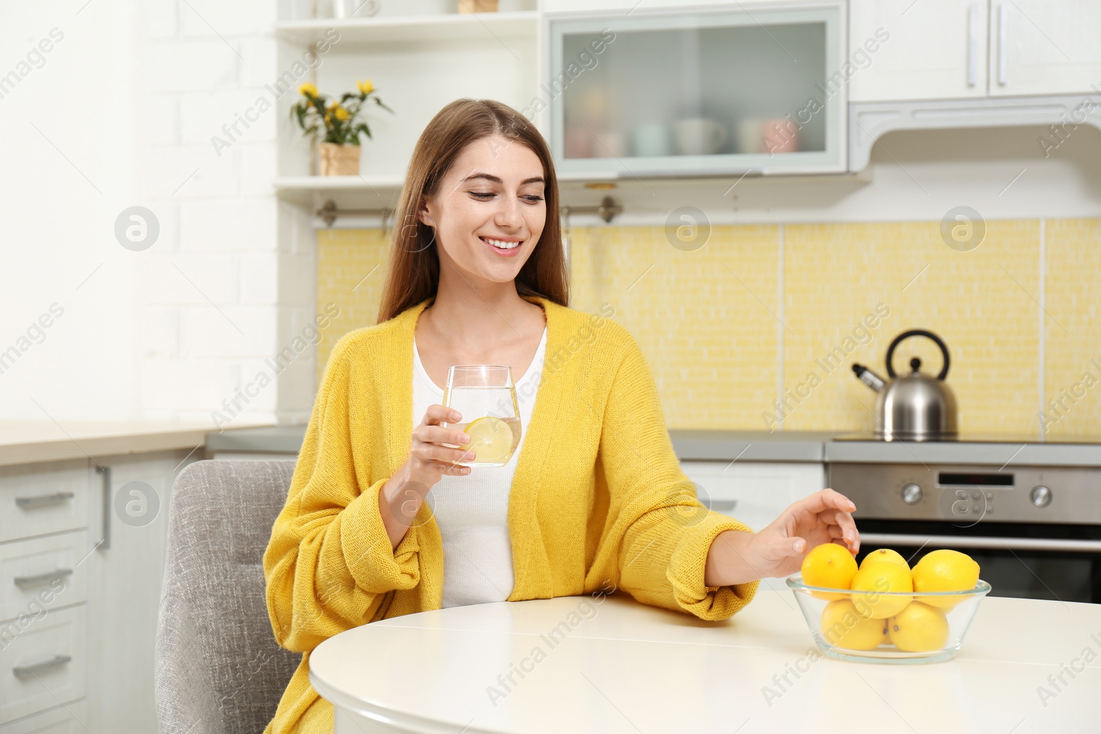 Photo of Young woman with glass of lemon water in kitchen