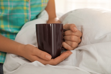 Photo of Woman with cup in bed at home, closeup