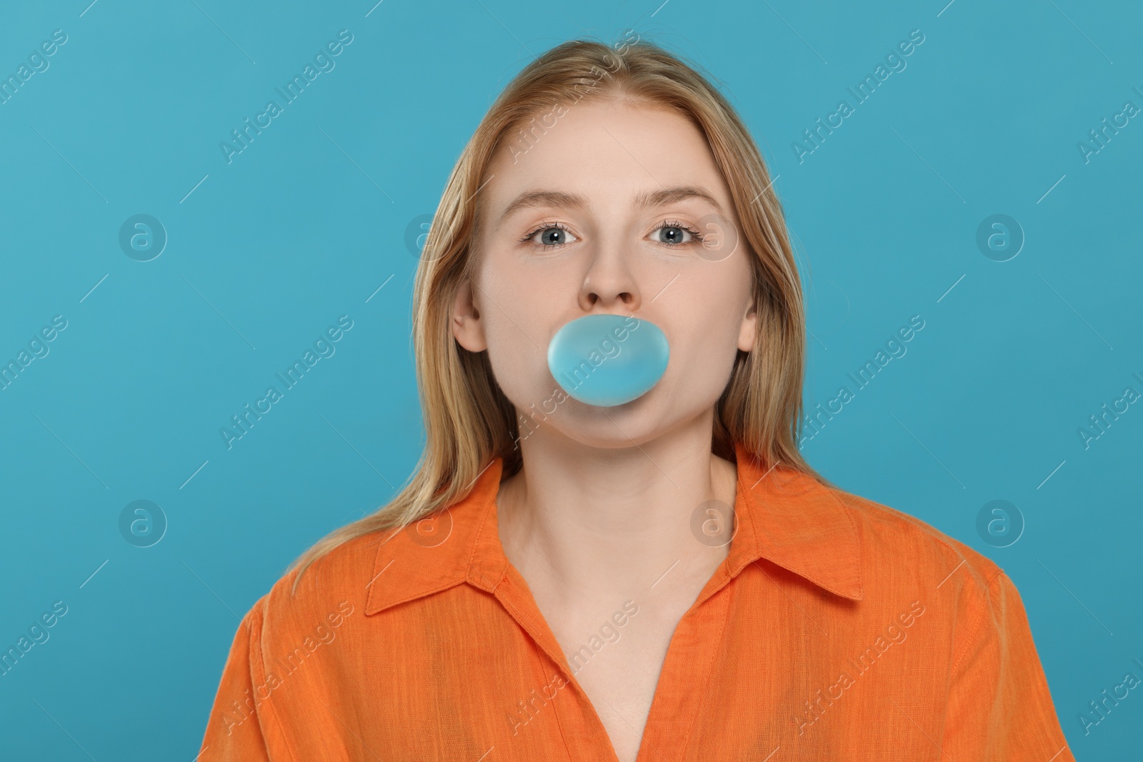 Photo of Beautiful young woman blowing bubble gum on light blue background