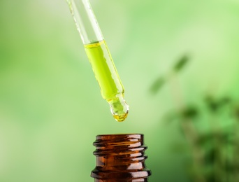 Photo of Dripping of essential oil into bottle on blurred background