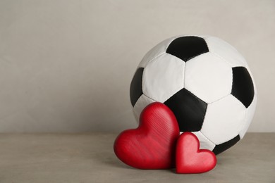 Photo of Soccer ball and hearts on grey table against light background. Space for text