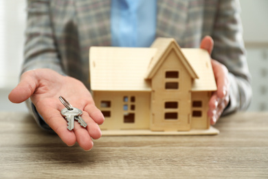 Real estate agent with house model and keys at wooden table, closeup