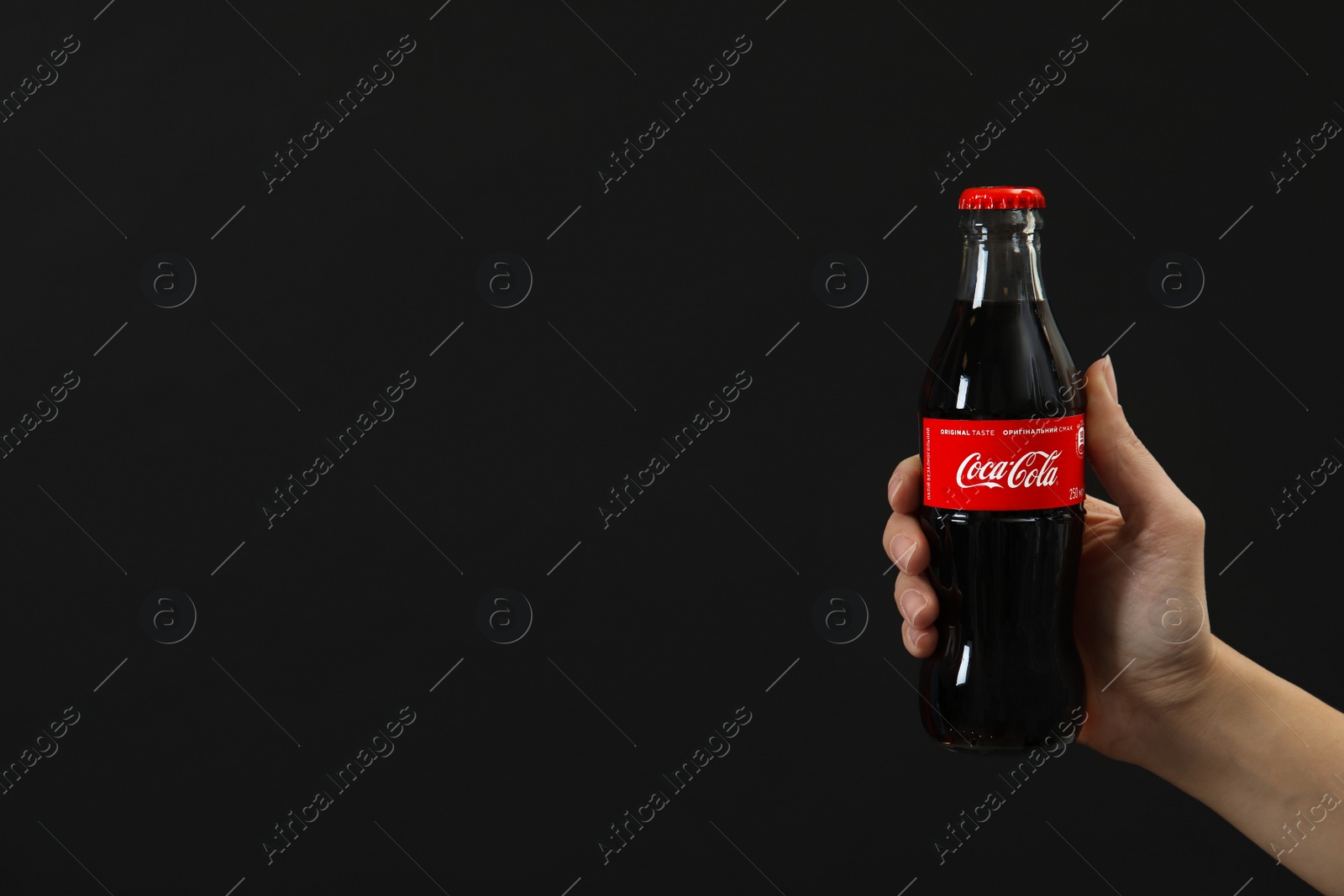 Photo of MYKOLAIV, UKRAINE - NOVEMBER 14, 2018: Woman holding bottle of Coca-Cola on black background. Space for text