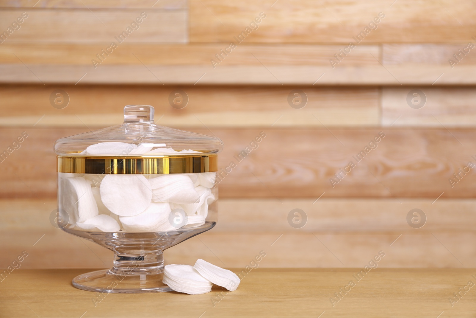 Photo of Composition of glass jar with cotton pads on table near wooden wall. Space for text