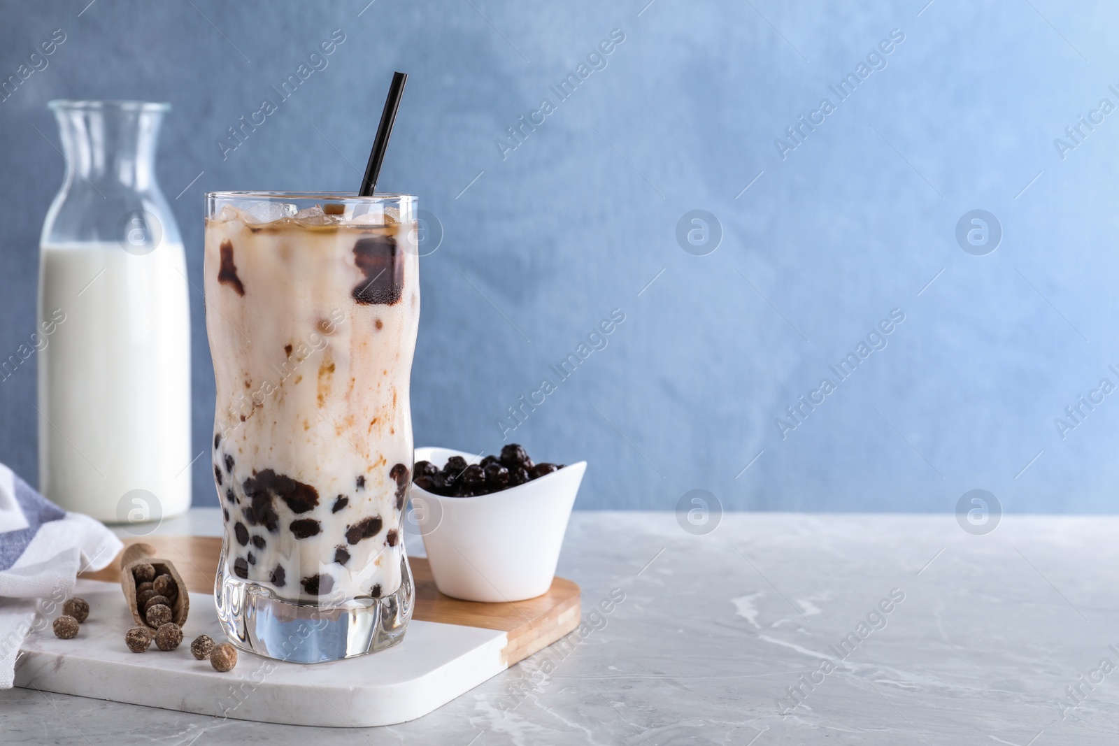 Photo of Bubble milk tea with tapioca balls on grey marble table against blue background. Space for text