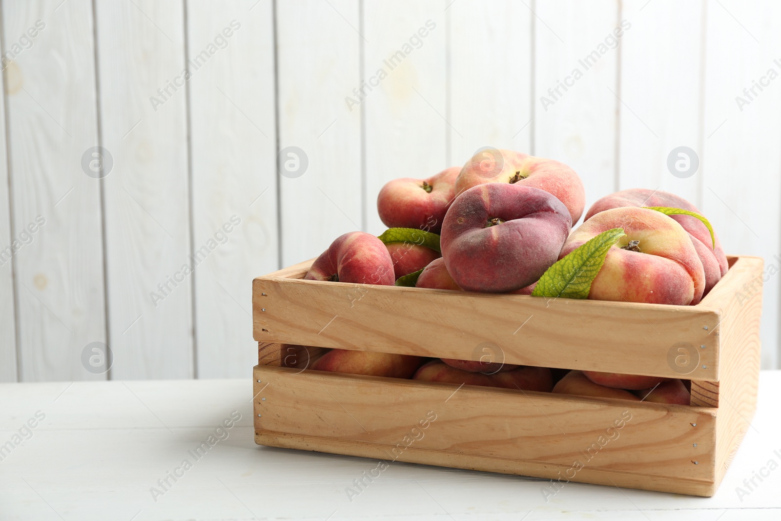 Photo of Fresh ripe donut peaches in crate on white wooden table