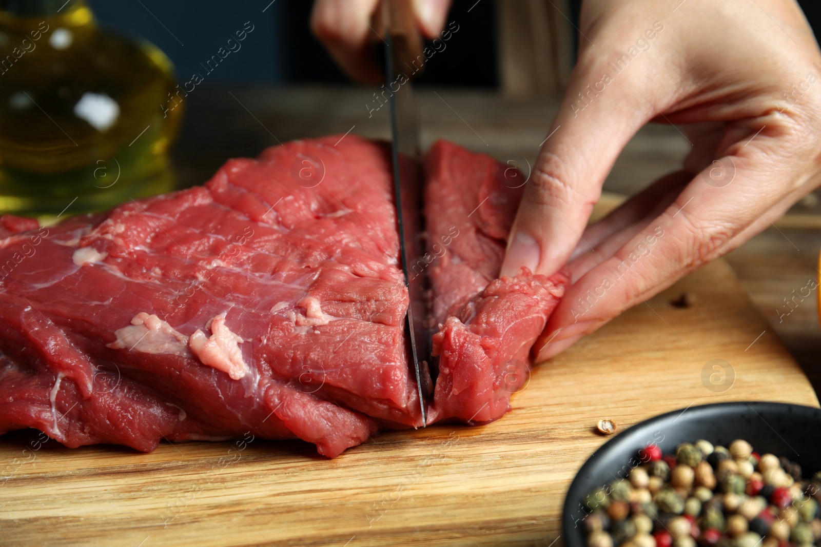 Photo of Woman cutting fresh raw meat at wooden table, closeup