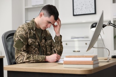 Photo of Military education. Young student in soldier uniform learning at wooden table in room