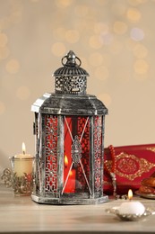 Photo of Arabic lantern, Quran, misbaha and candles on wooden table against blurred lights