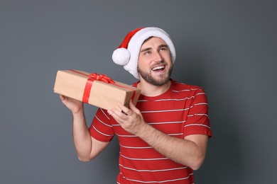 Young man with Christmas gift on grey background