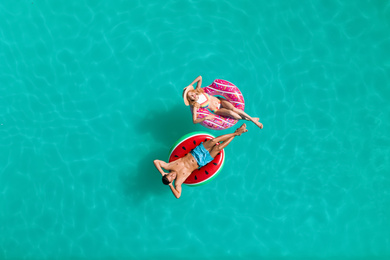 Happy couple with inflatable rings in swimming pool, top view. Summer vacation