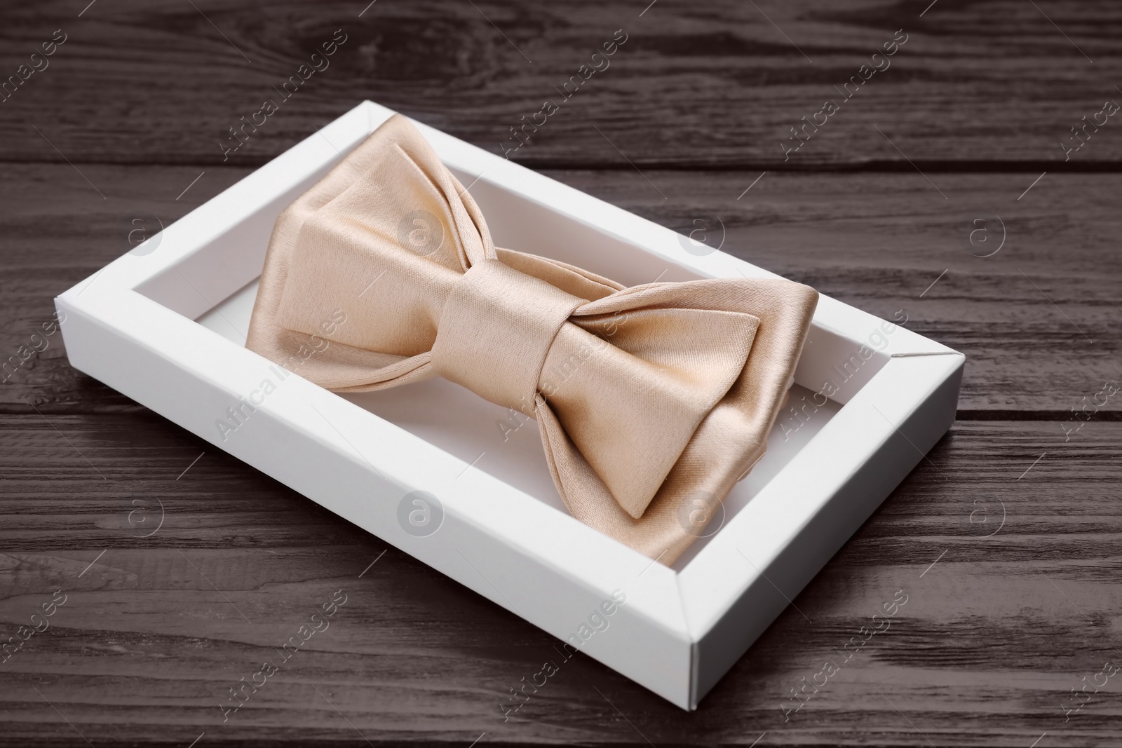 Photo of Stylish beige bow tie in box on wooden table, closeup